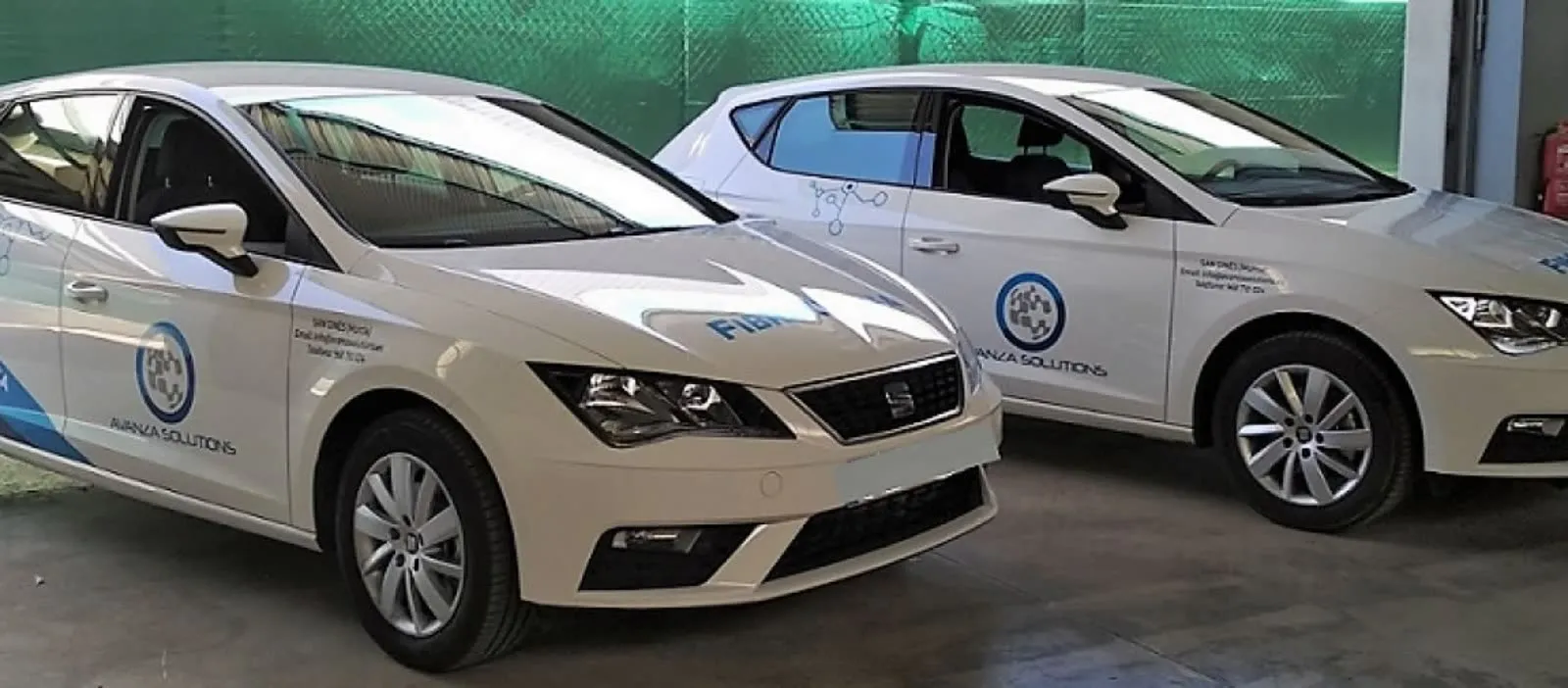 Dos coches blancos rotulados con el logotipo de Avanza Solutions aparcados en una nave