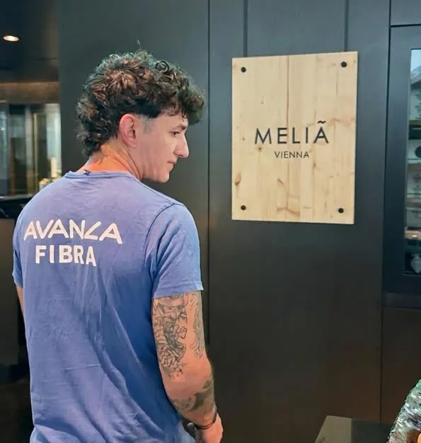 Técnico de espaldas, con camiseta de Avanza Fibra, ante el rótulo de Meliá Vienna en la entrada del hotel