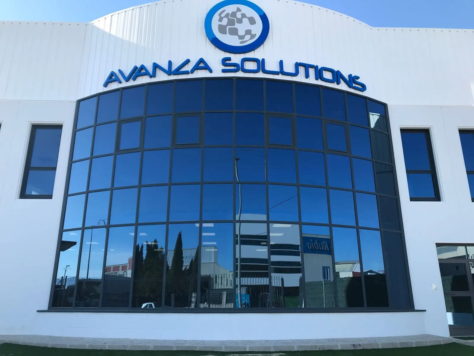 Fachada blanca de la sede de Avanza Solutions, con el logotipo sobre un gran ventanal de cristal azul